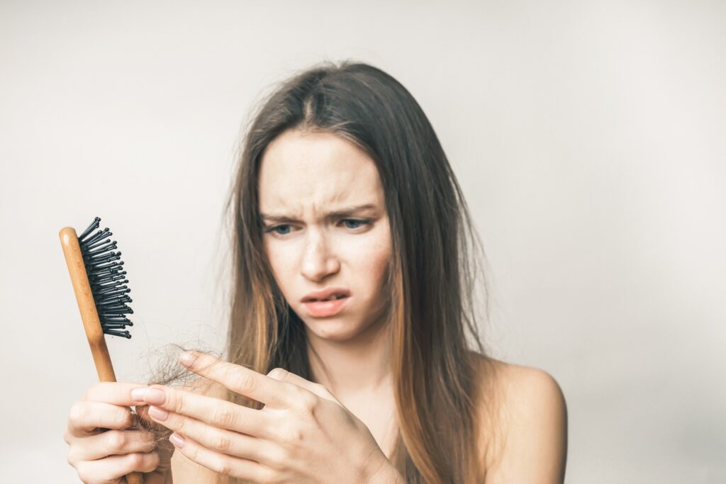 Kobieta trzyma w ręku szczotkę i dużą ilość włosów, które wypadły
