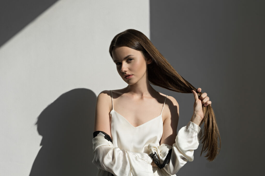 Młoda dziewczyna trzyma w dłoni swe długie, zadbane i mocne brązowe włosy