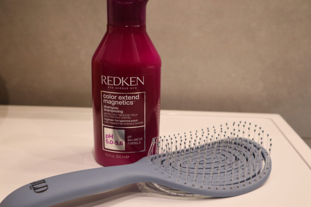 Szampon Redken Color Extend Magnetics stojący obok szczotki do włosów