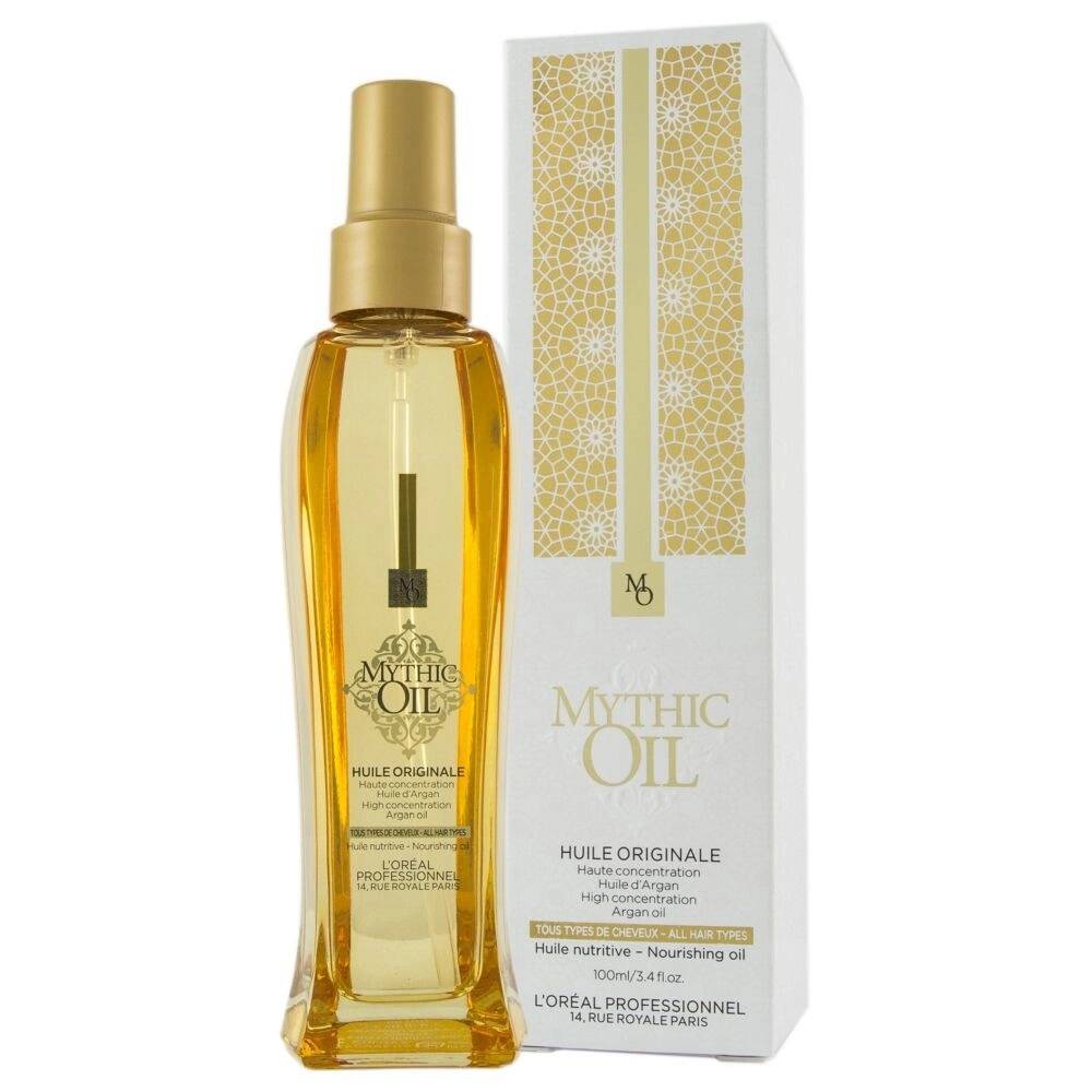Butelka złotego olejku Mythic Oil stoi obok ozdobnego białego pudełka kosmetycznego.