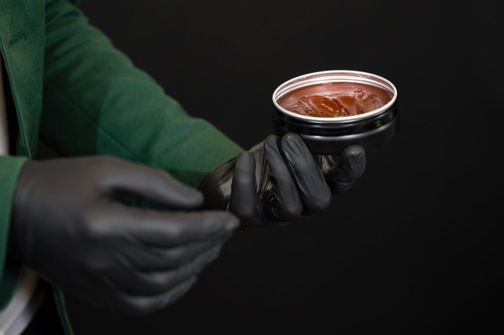 Mężczyzna w czarnych rękawiczkach trzyma opakowanie pomady do włosów