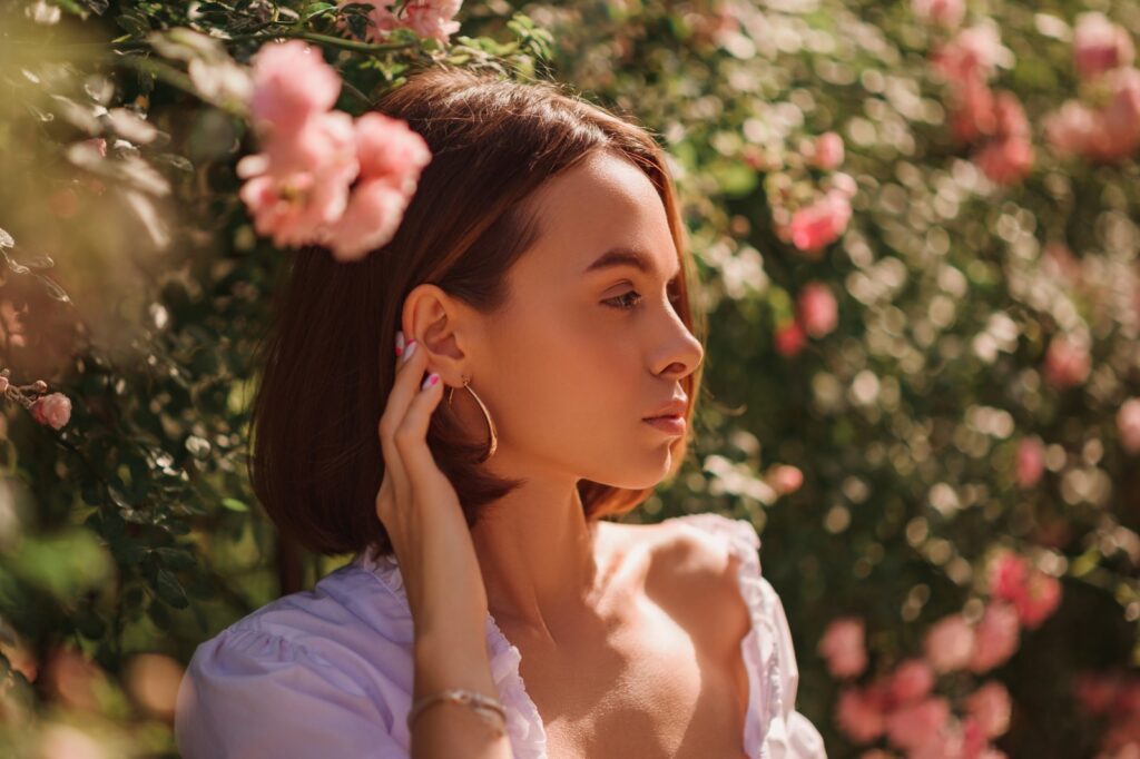 Młoda kobieta na dworze dotyka ucha dłonią i ma fryzurę w stylu jawline bob