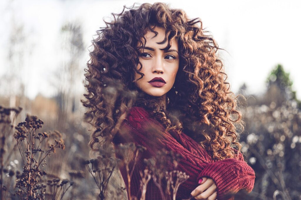 Brunetka z włosami w stylu fluffy curls pozuje do zdjęcia na dworze w jesiennej atmosferze