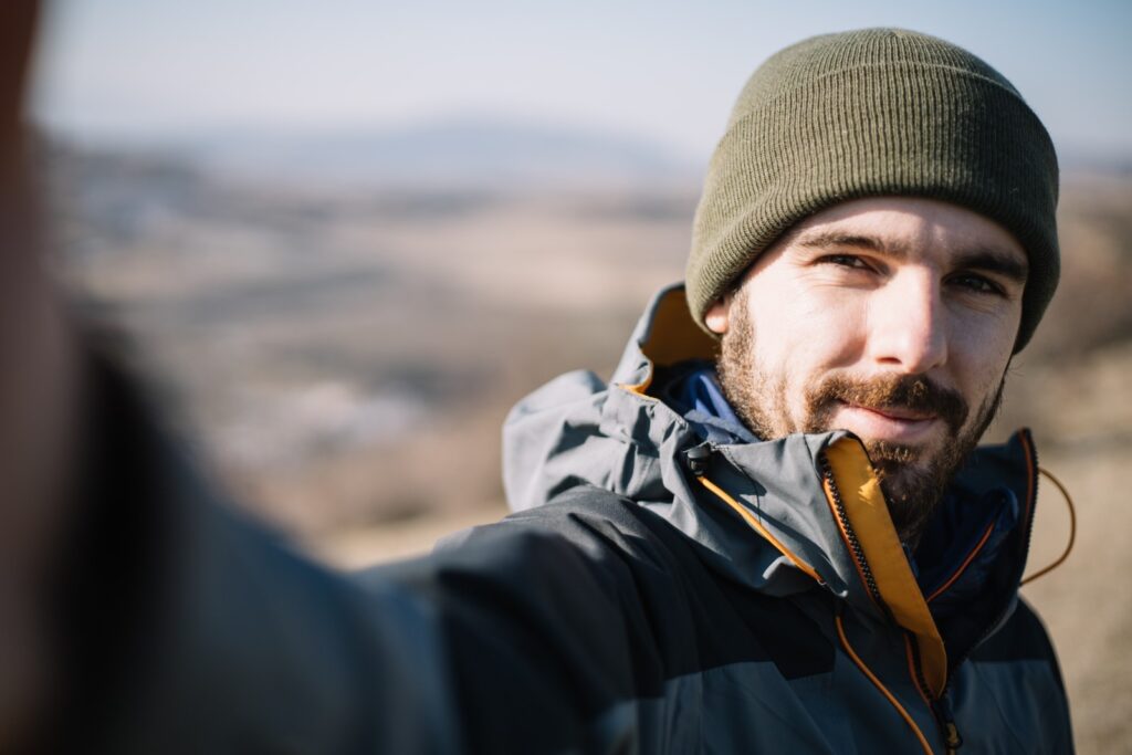 Mężczyzna robiący selfie w czapce i z krótką, trochę rzadką brodą