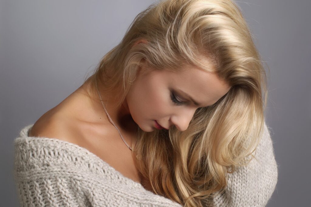 Portret kobiety w jasnym swetrze i ciepłymi, długimi blond włosami