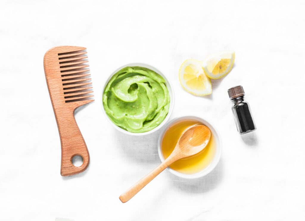 Składniki do domowej maski do włosów: awokado, miód, cytryna, olejek, obok drewniany grzebień