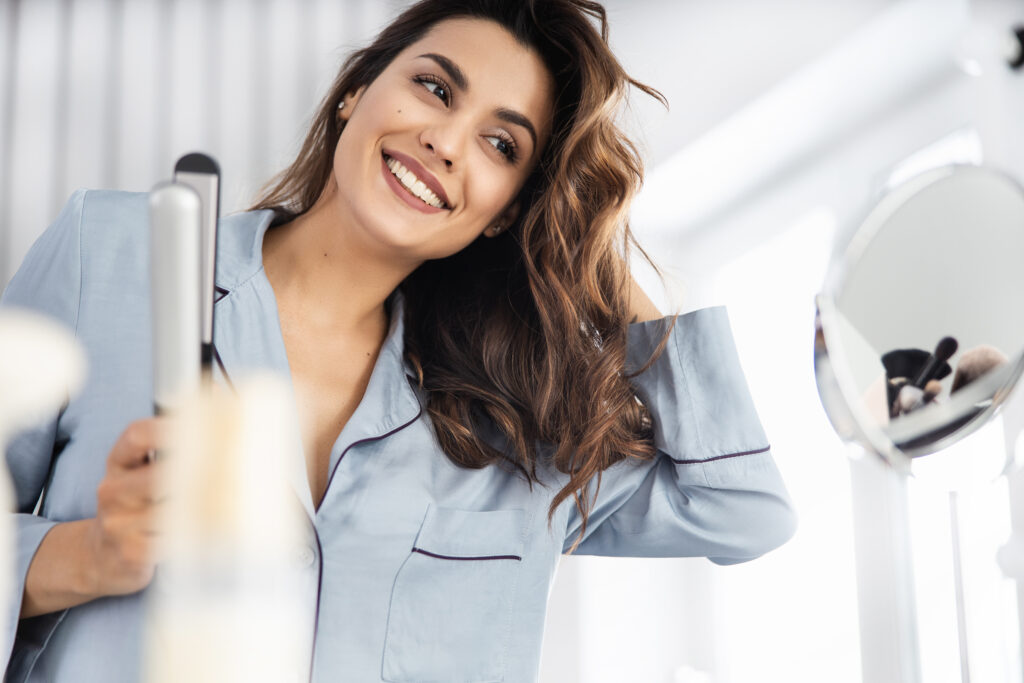 ALT: Uśmiechnięta kobieta w piżamie w łazience ocenia swoje włosy