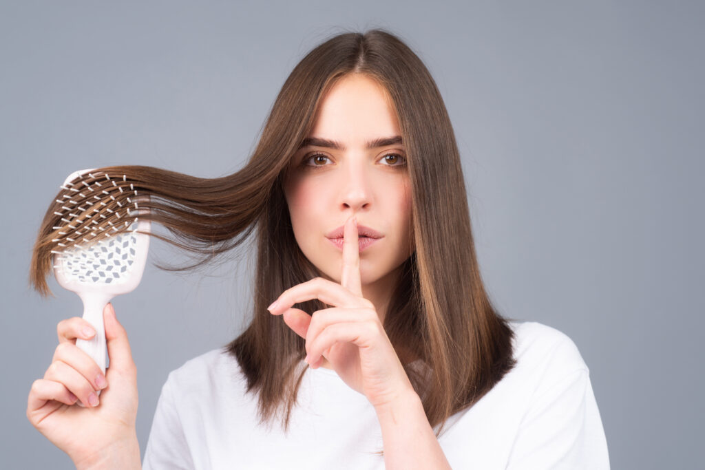 Kobieta prezentuje idealnie gładkie pasma włosów i wskazuje palcem gest sekretu