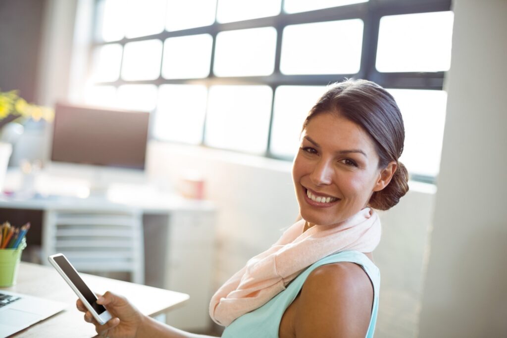 Kobieta w biurze z telefonem w dłoni i fryzurze sleek bun