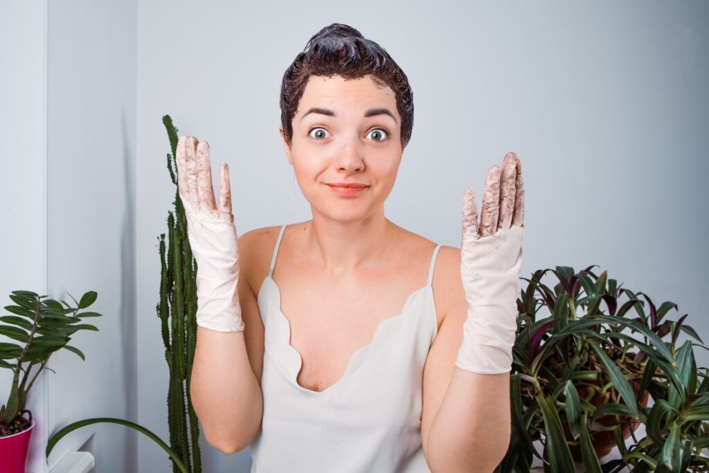 Lekko zdumiona młoda kobieta z farbą na włosach i w brudnych jednorazowych rękawiczkach