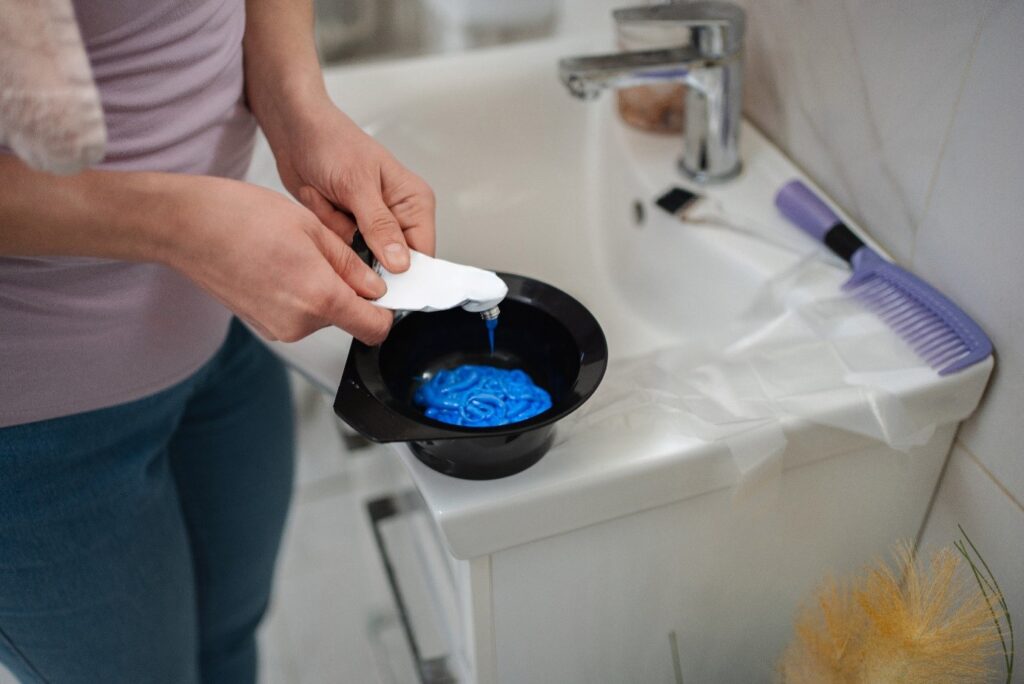 Kobieta w łazience wyciska niebieską farbę do włosów do czarnej plastikowej miseczki