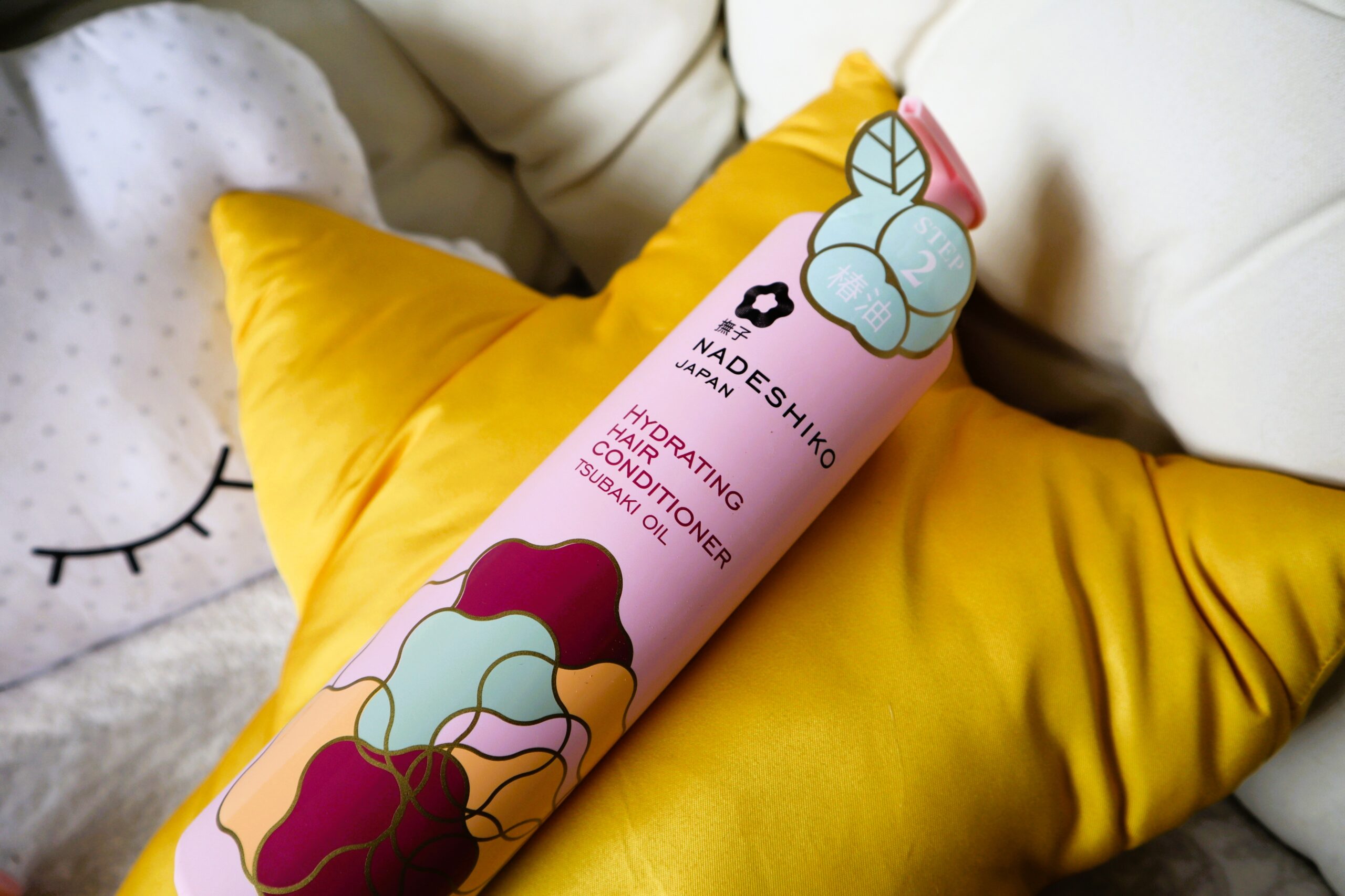 Nadeshiko odżywka nawilżająca do włosów leżąca butelka na żółtej poduszce