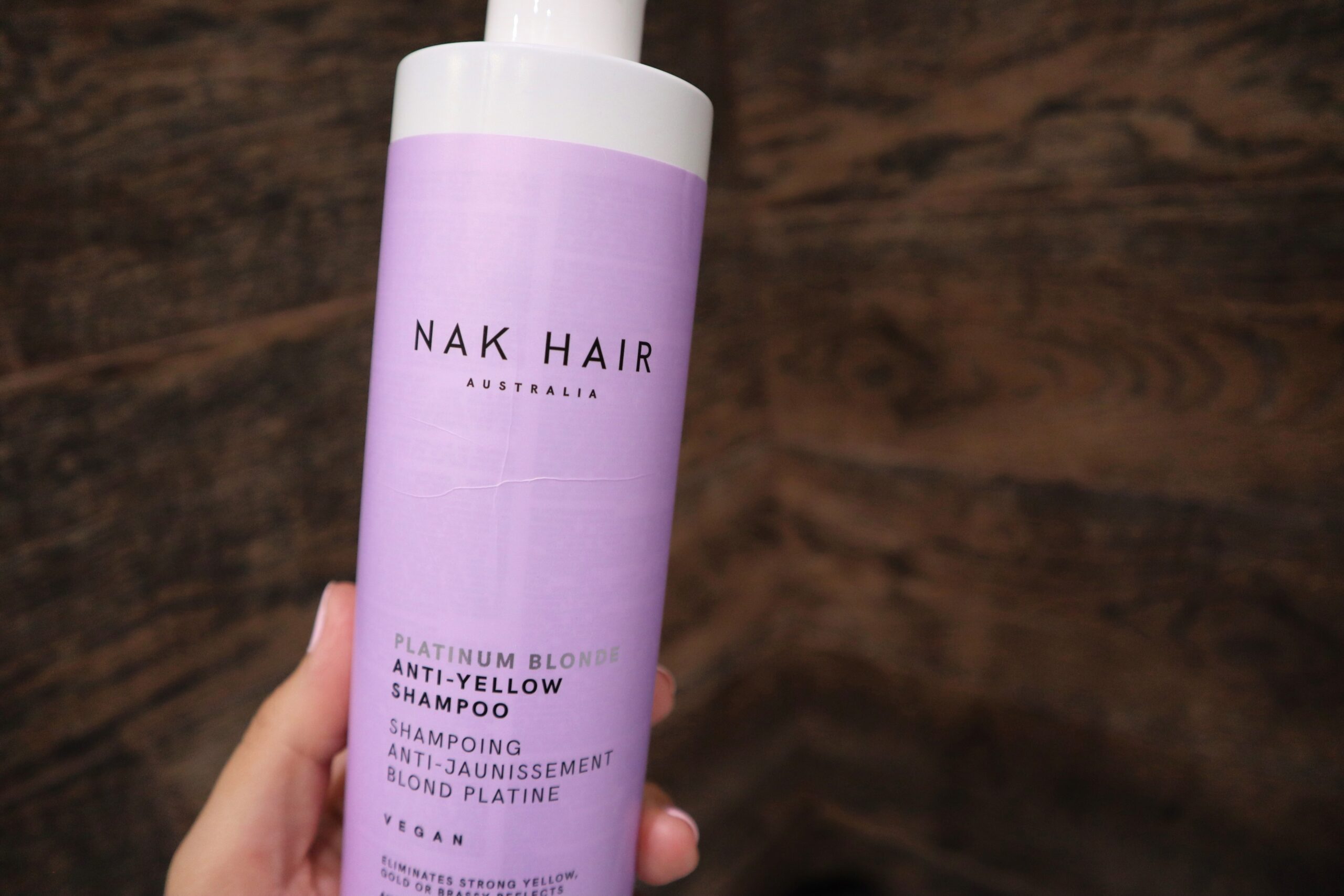 Szampon tonujący NAK Platinum Blonde na tle brązowych płytek w łazience