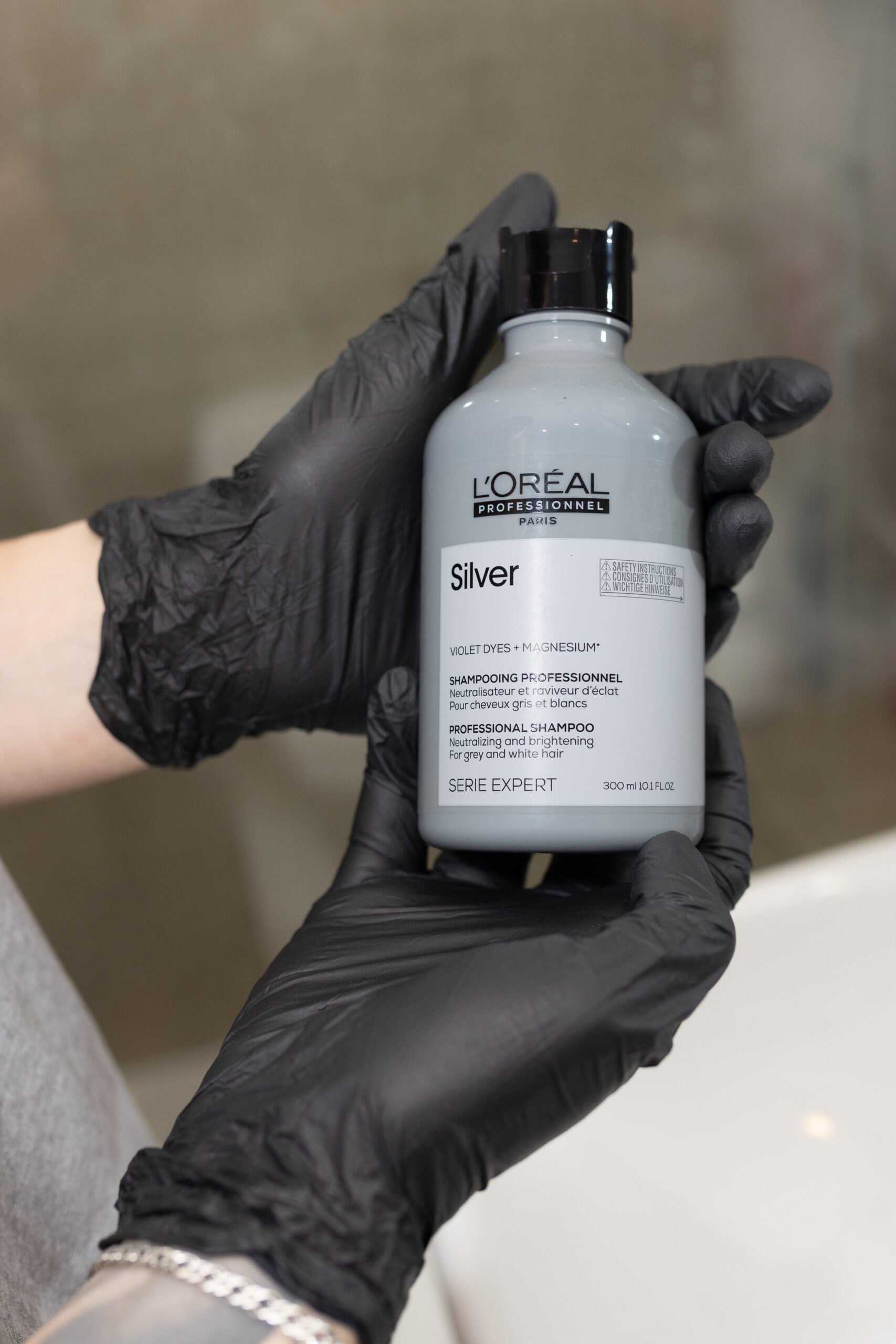 Kobiece dłonie w rękawiczkach ochronnych trzymają butelkę szamponu do siwych włosów L'Oréal Professionnel Silver