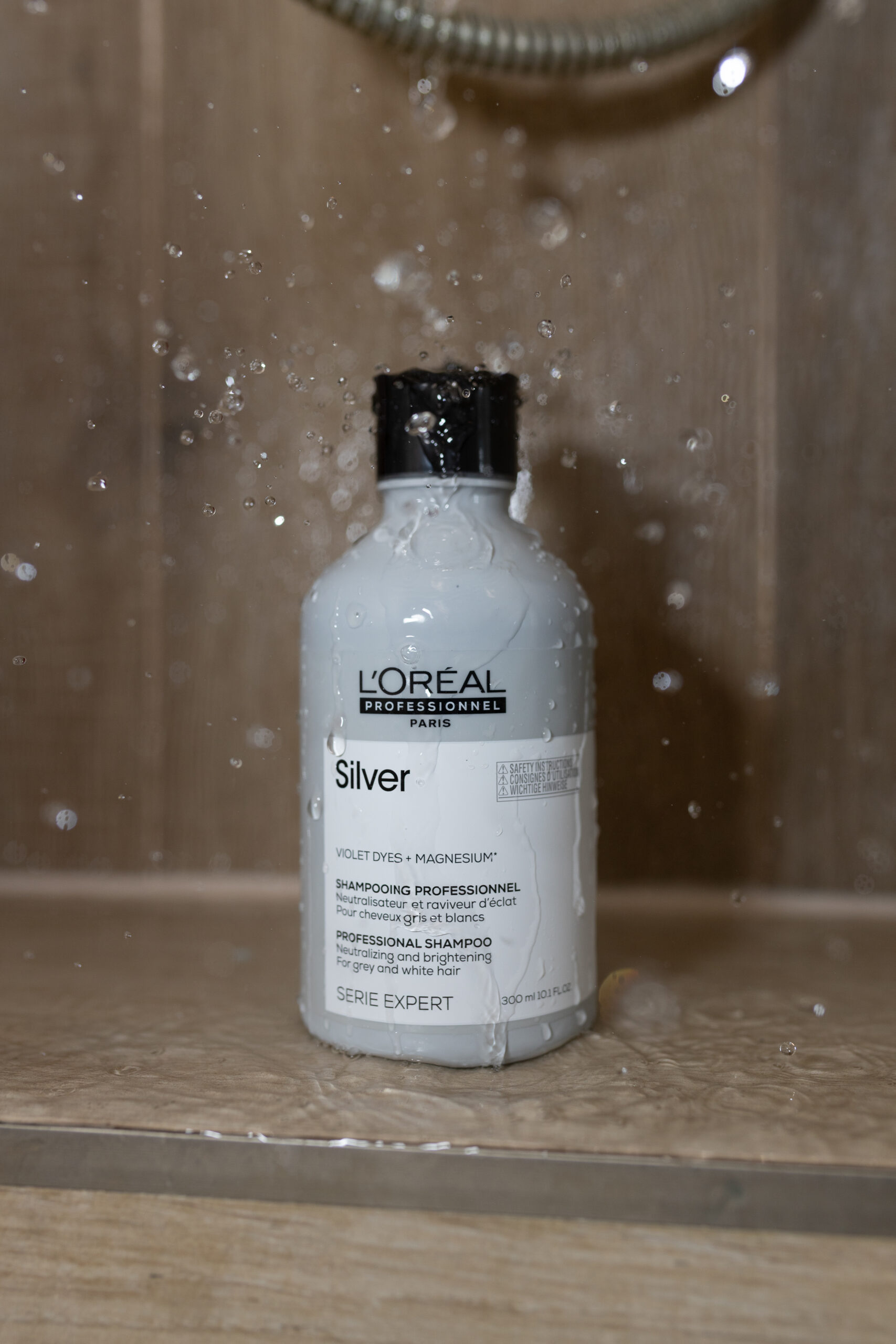 Kobiece dłonie w rękawiczce aplikują fioletowy szampon do siwych włosów L'Oréal Professionnel Silver na dłoń