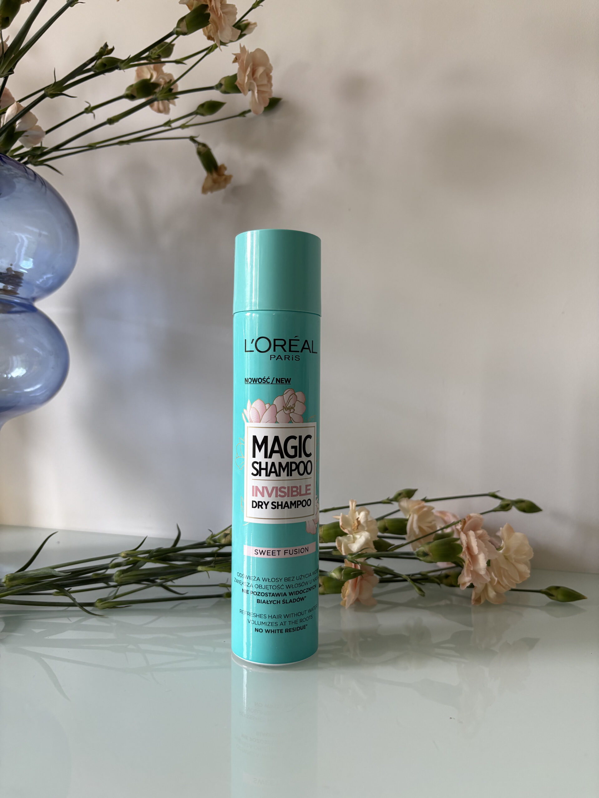 Suchy szampon do włosów L'Oréal Paris Sweet Fusion na tle suszonych kwiatów i dzbanka z kwiatami