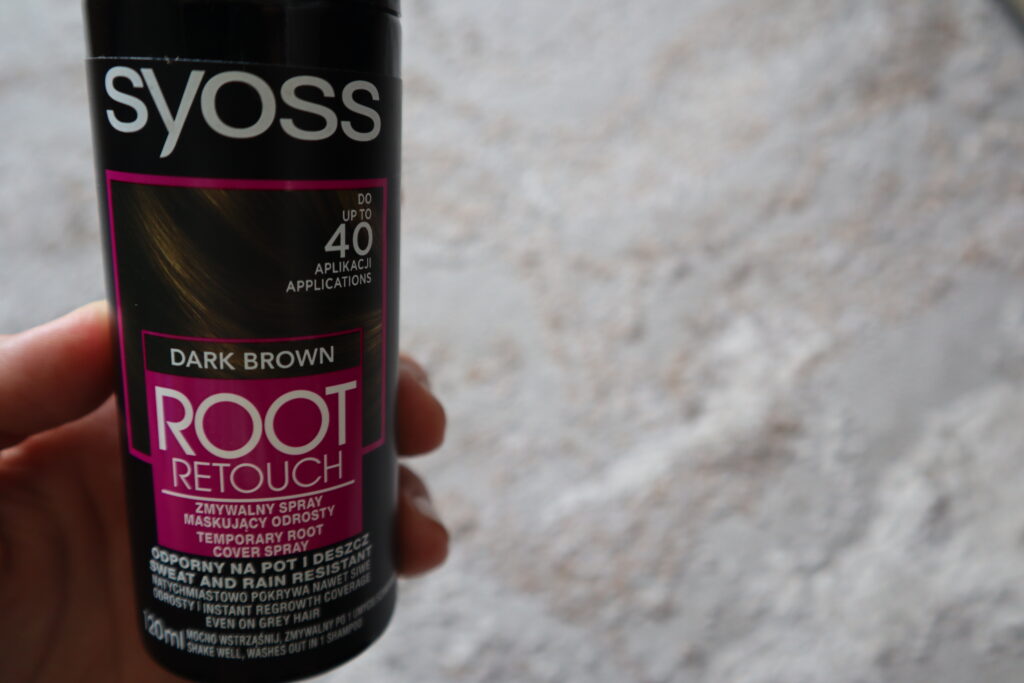 Kobieca dłoń trzymająca Syoss Root Retouch zmywalny spray do odrostów ciemny brąz