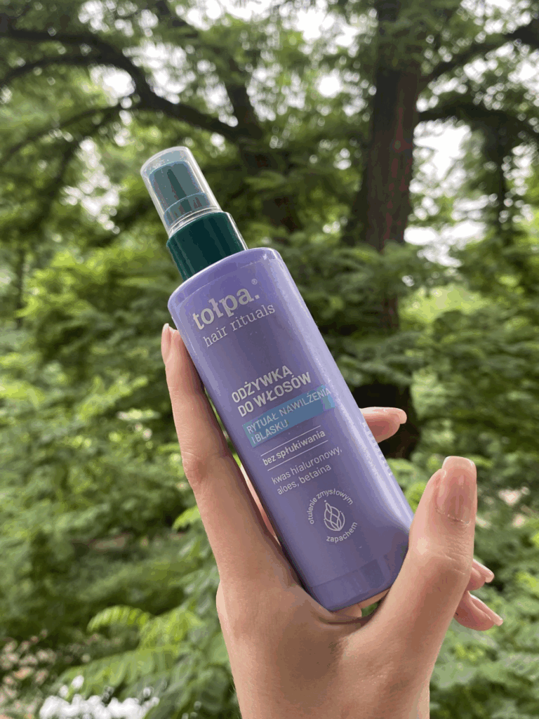 Kobieca dłoń trzymająca odżywkę bez spłukiwania Tołpa Hair Rituals, w tle park