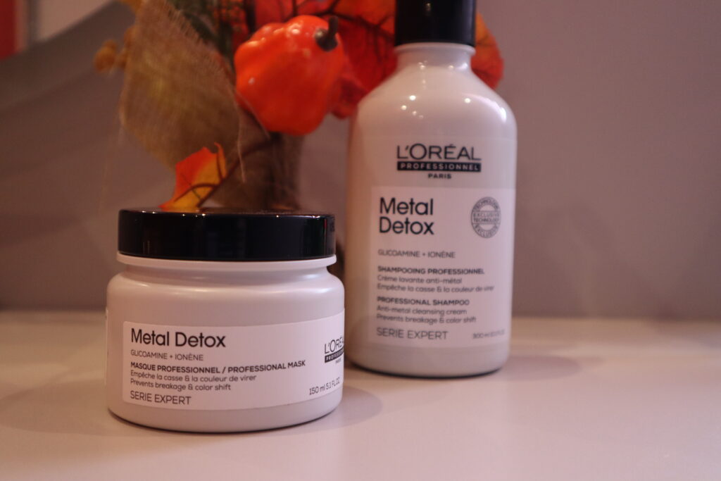 Opakowanie maski i szamponu z serii L'Oreal Professionnel Metal Detox do włosów po zabiegu farbowania na tle jesiennych dekoracji