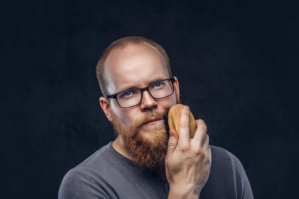 Mężczyzna w okularach używa kartacza do brody, ciemne tło