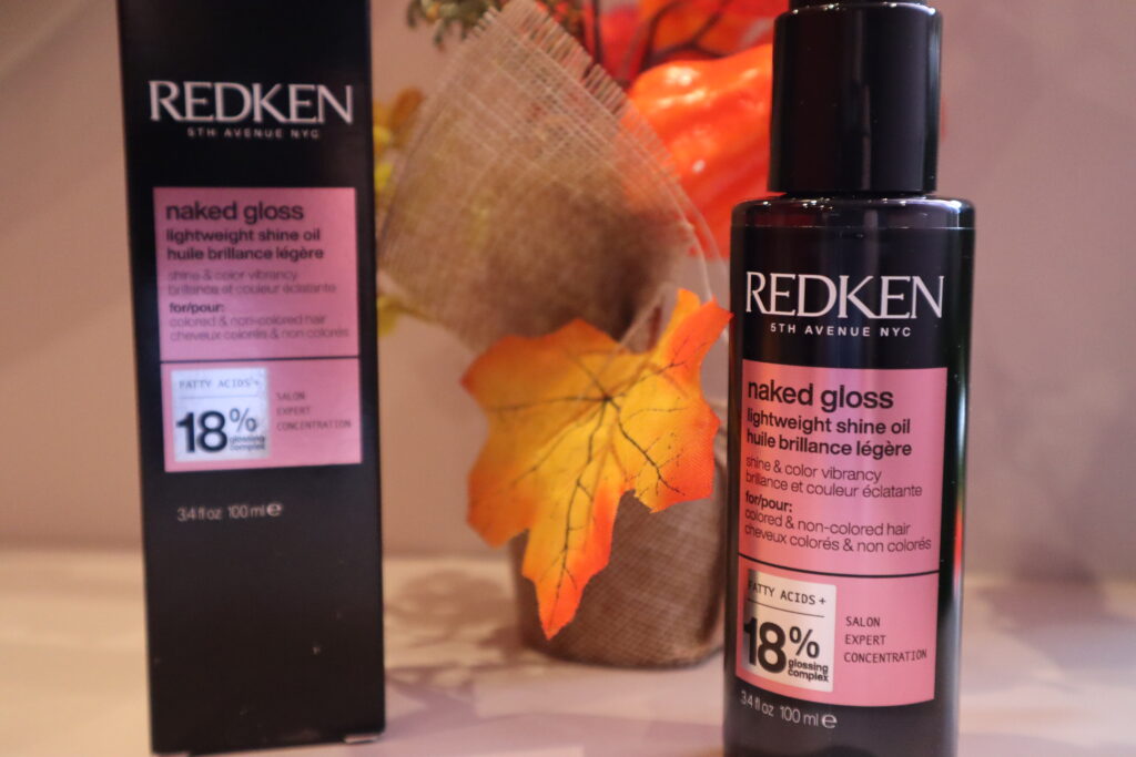Olejek nabłyszczający do włosów farbowanych REDKEN Naked Gloss : papierowy kartonik i wyjęte opakowanie plastikowe na tle jesiennych dekoracji