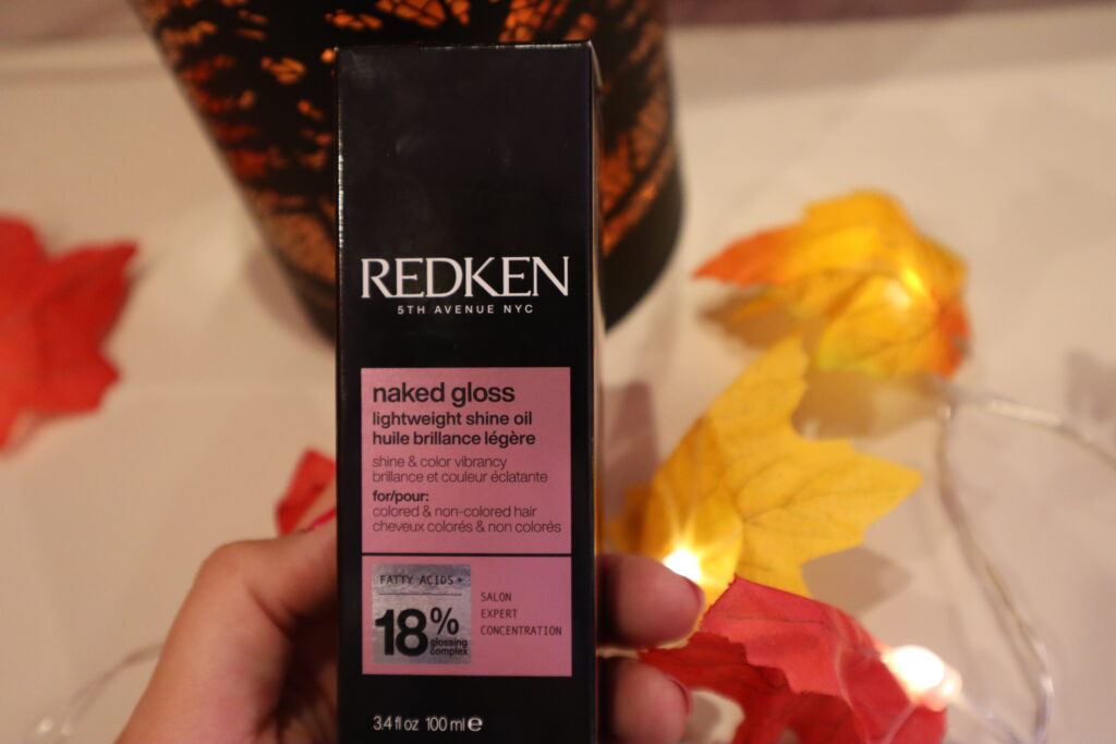 Kobieca dłoń trzyma opakowanie olejku do włosów farbowanych REDKEN Naked Gloss