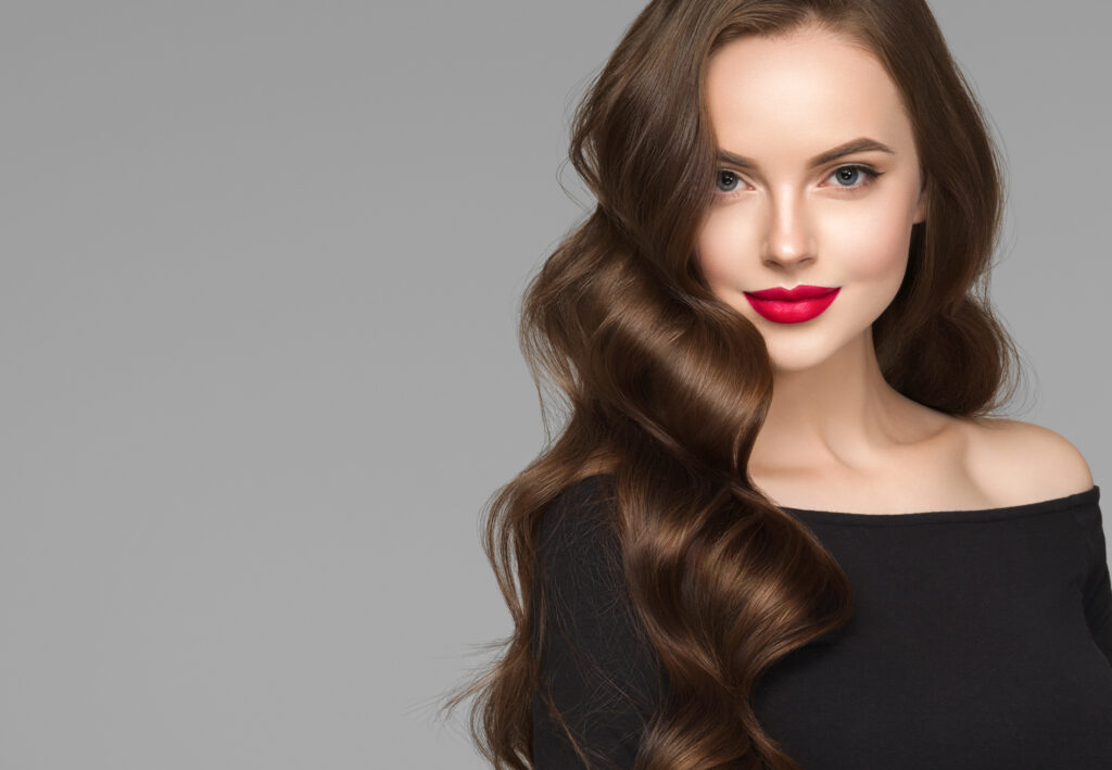 Młoda kobieta o jasnej karnacji i z długimi, brązowymi włosami na szarym tle