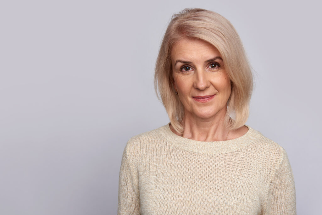 Kobieta w średnim wieku o jasnych włosach wpadających w truskawkowe tony. Kolor włosów ją odmładza, dodaje energii oraz podkreśla jej ciemną oprawę oczu
