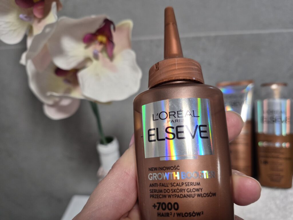 Kobieca dłoń trzyma opakowanie serum do skóry głowy przeciw wypadaniu włosów L’Oreal Paris Elseve Growth Booster