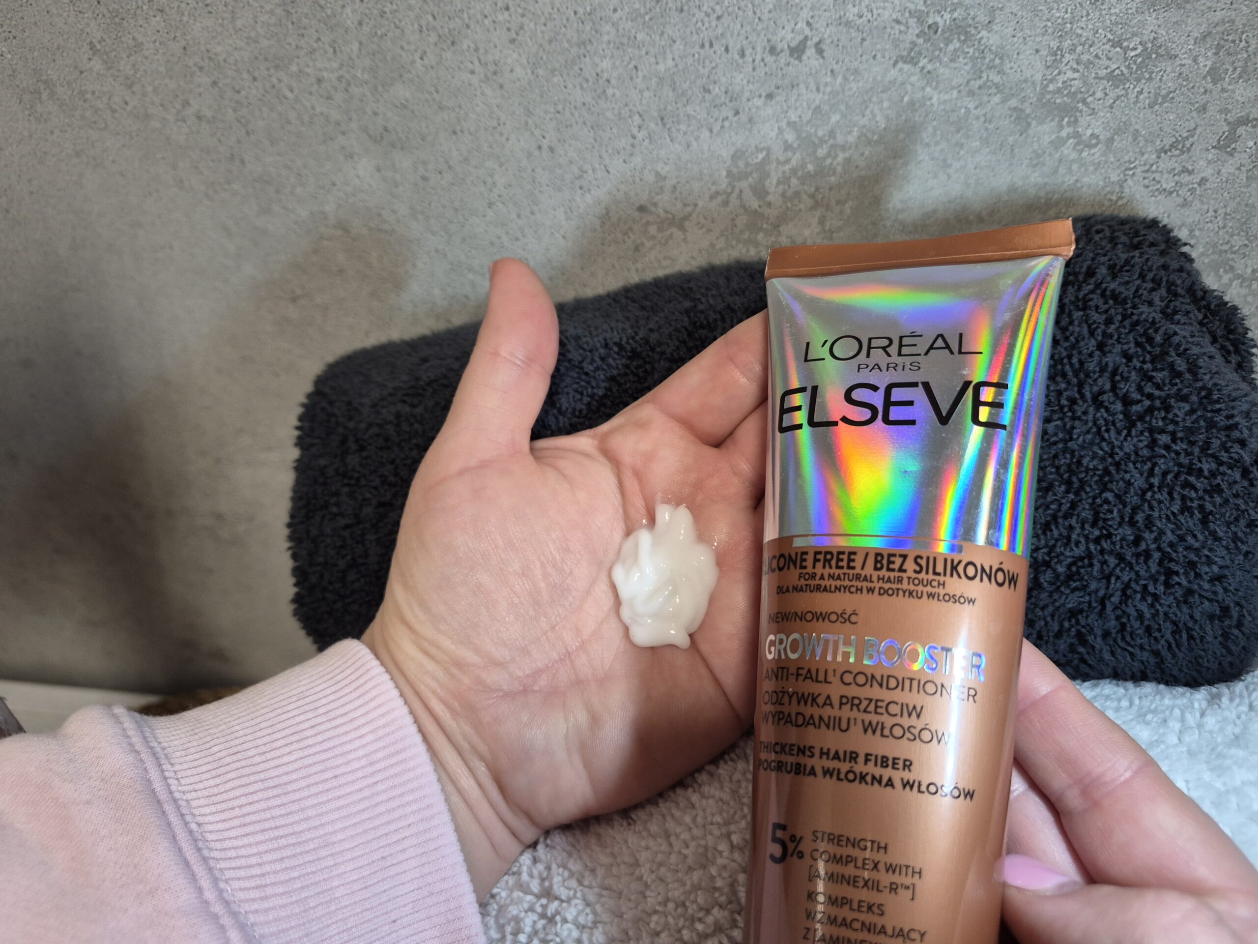 Kobieca dłoń trzyma odżywkę do wypadających włosów L’Oreal Paris Elseve Growth Booster