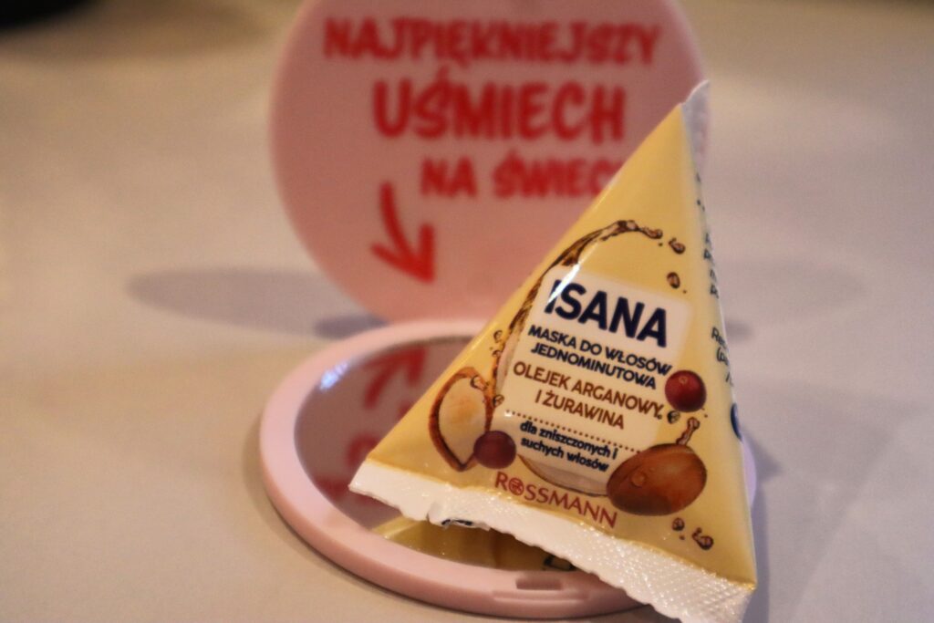 Żółta maska do włosów jednominutowa olejek arganowy i żurawina Isana, w tle lusterko z Rossmana