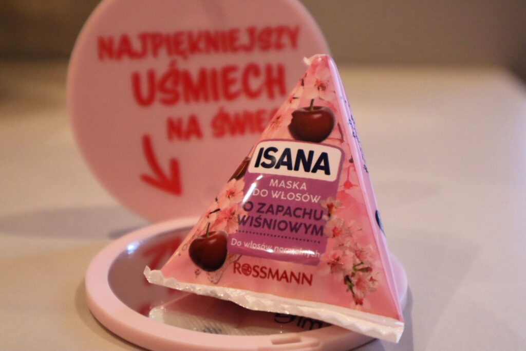 Opakowanie maski do włosów normalnych o zapachu wiśniowym Isana, w tle lusterko z Rossmana