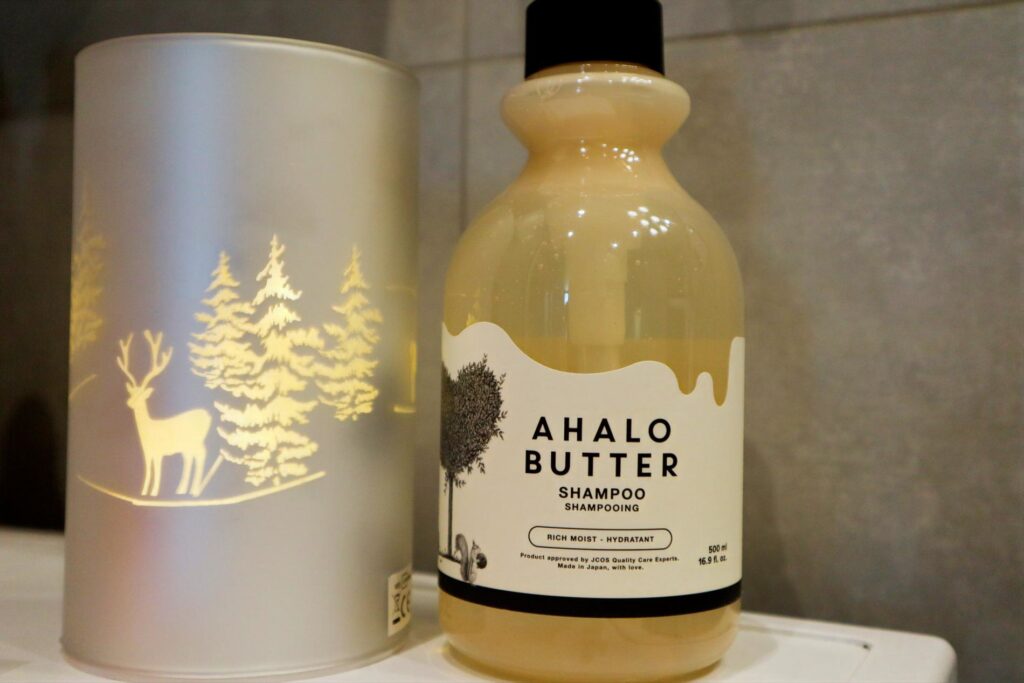 Butelka Ahalo Butter Nawilżająco-odżywczy szampon do włosów obok ozdobnej lampki w łazience