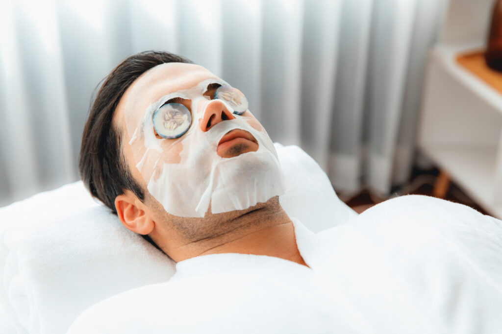 Mężczyzna w maseczce w płachcie, z plastrami ogórka na oczach