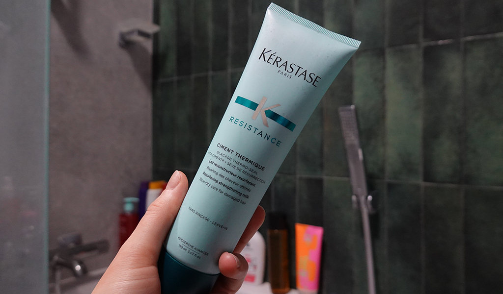 Dłoń trzymająca tubkę Kérastase Resistance Ciment Thermique w łazience - zdjęcie