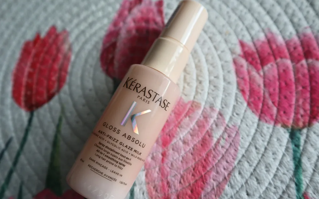 Wielofunkcyjne mleczko do długich puszących się włosów Kérastase Gloss Absolu Anti-Frizz Glaze Milk 45 ml na tle dekoracyjnej podkładki na stole