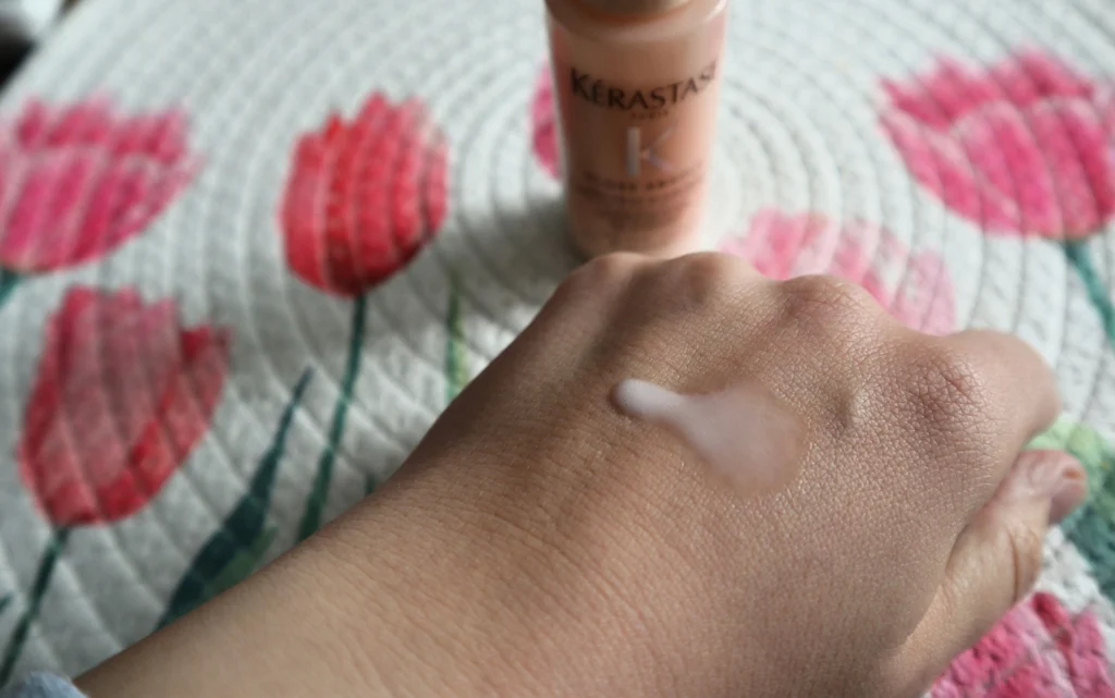 Wielofunkcyjne mleczko do długich puszących się włosów Kérastase Gloss Absolu Anti-Frizz Glaze Milk aplikacja na kobiecej dłoni