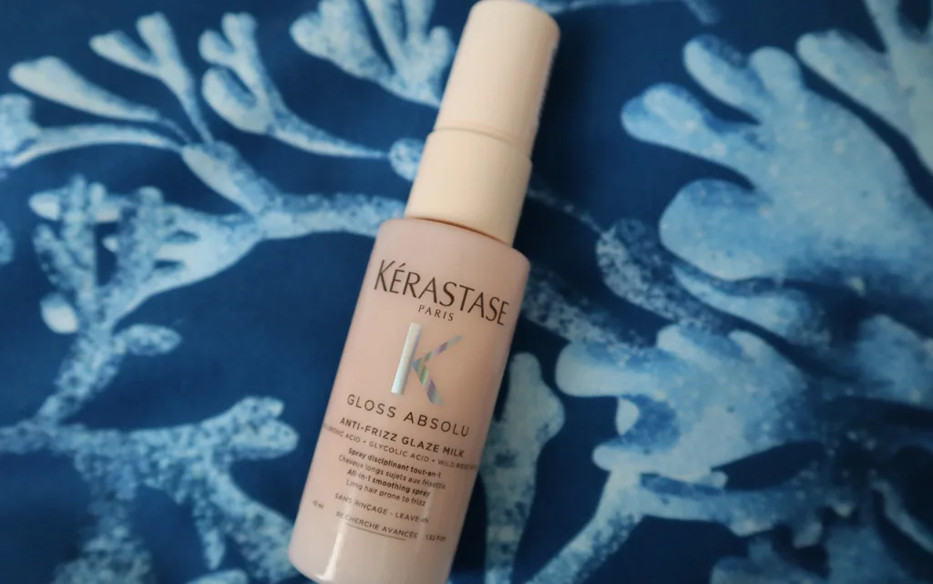 Wielofunkcyjne mleczko do długich puszących się włosów Kérastase Gloss Absolu Anti-Frizz Glaze Milk 45 ml na tle niebieskiej poduszki