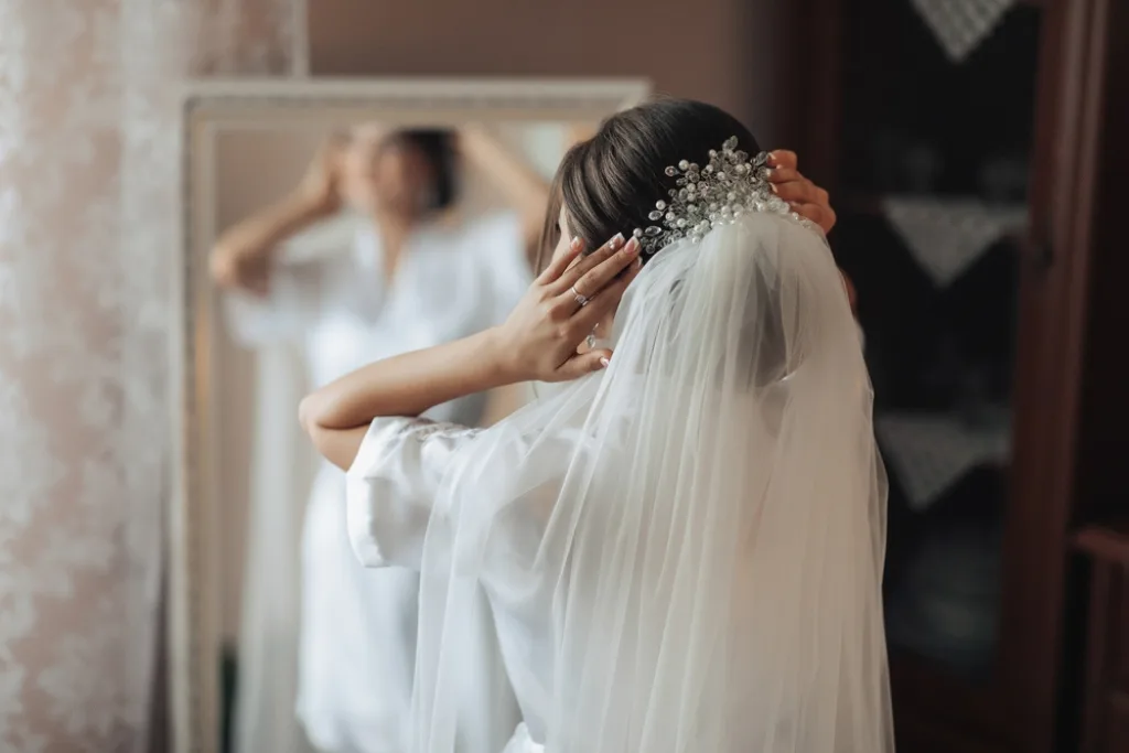 Panna młoda przed lustrem przymierza welon na ułożoną fryzurę