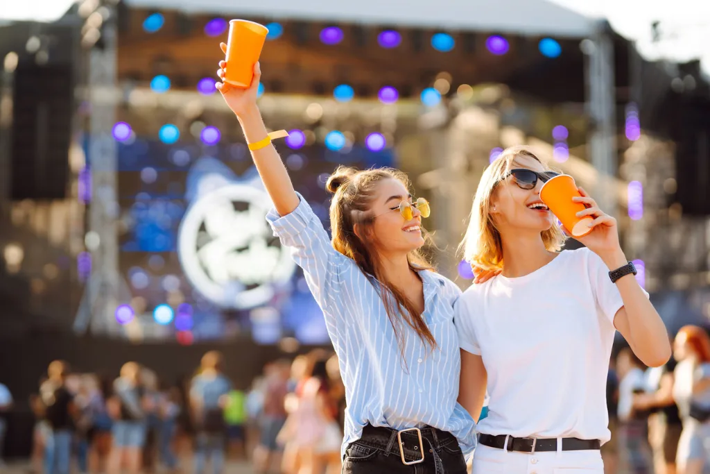 Dwie młode kobiety na festiwalu muzycznym pijące chłodne napoje nw dworze