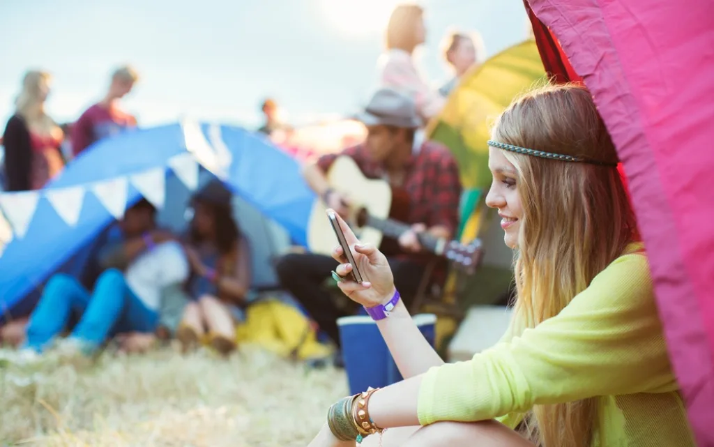 Usmiechnięta dziewczyna w stylu hipiski pisze sms podczas festiwalu muzycznego