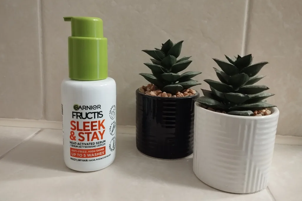 Serum na puszące się włosy Garnier Fructis Keratin Sleek & Stay w łazience, obok ozdobne kwiatki w doniczce