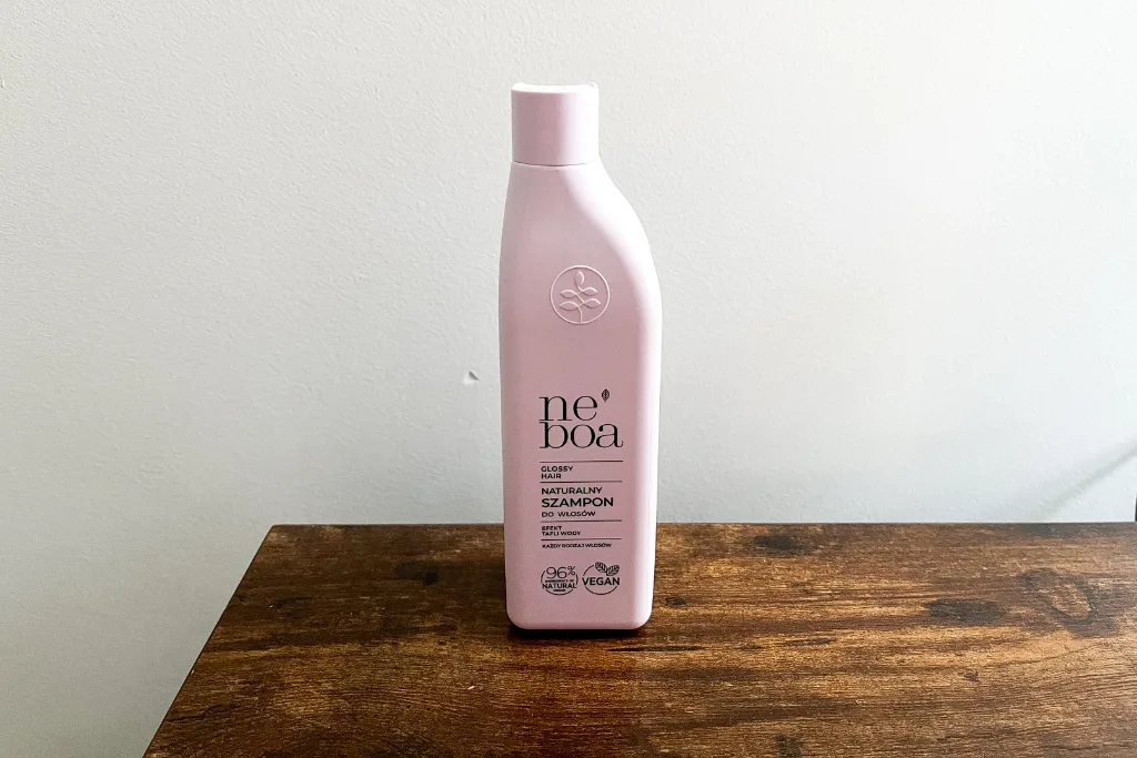 Neboa Glossy Hair naturalny szampon do włosów stojący na brązowym stole na tle białej ściany