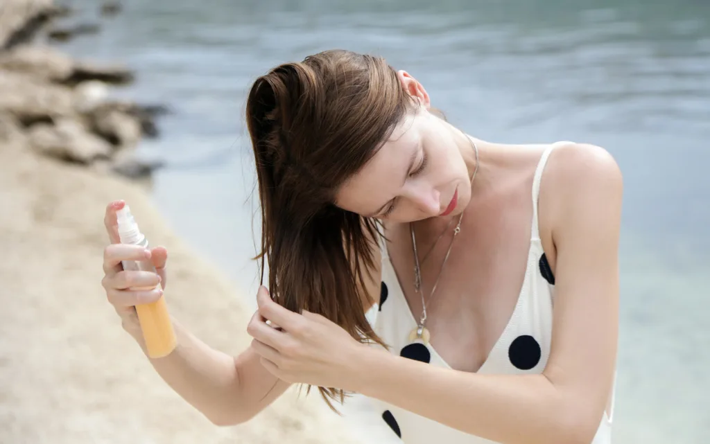 Brunetka na plaże aplikuje spray z SPF na włosy
