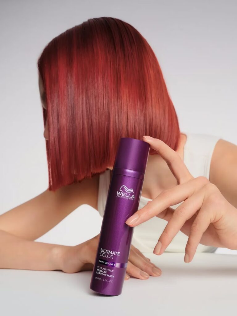 Kobieta z czerwonymi włosami pokazuje kosmetyk Wella Proffesional Ultimate Color