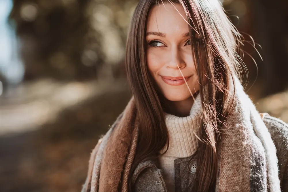 Usmiechnięta brunetka z długimi włosami na dworze na jesiennym spacerze