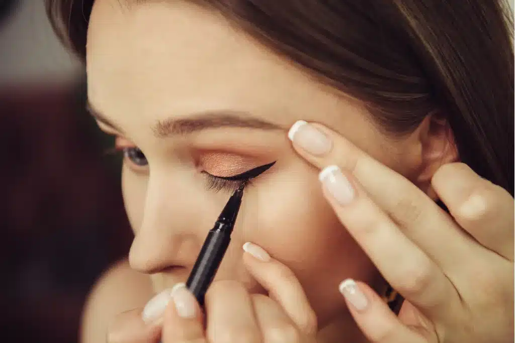 Kobieta rysuje kreskę eyelinerem, tworząc kocie oko