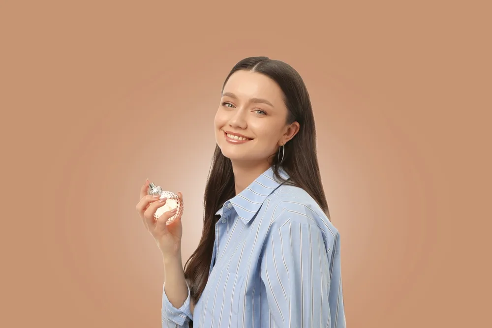 Kobieta szczęśliwie pozuje z butelką perfum w ręku